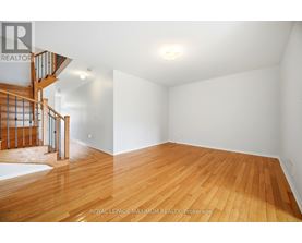 A spacious room with wooden flooring and a staircase on the left side.