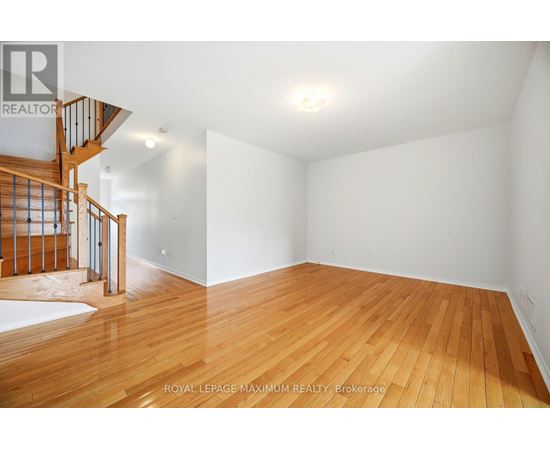 A spacious room with wooden flooring and a staircase on the left side.