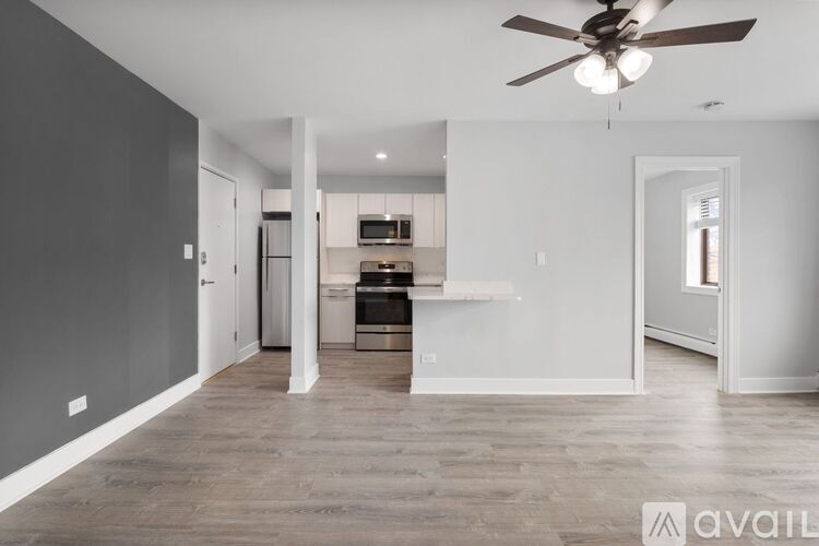 A spacious living room with a ceiling fan and a kitchen area in the background.