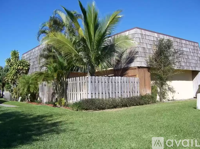 A house with a wooden fence and palm trees in front.