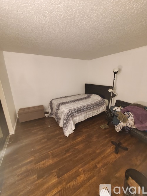 A bedroom with a bed, wooden floor, and a wall-mounted lamp.