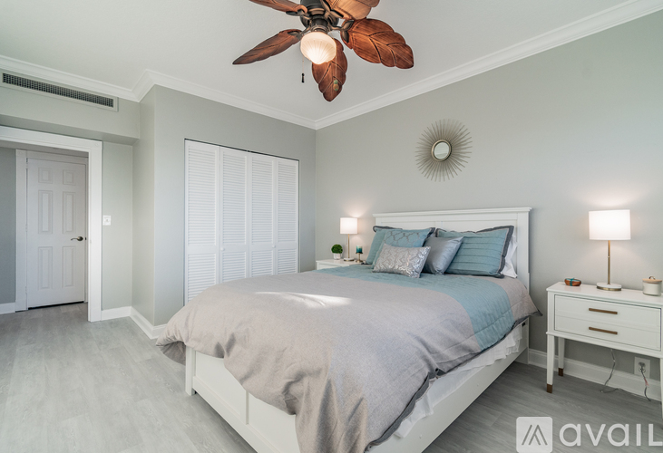 A bedroom with a bed, a ceiling fan, and a nightstand with a lamp.