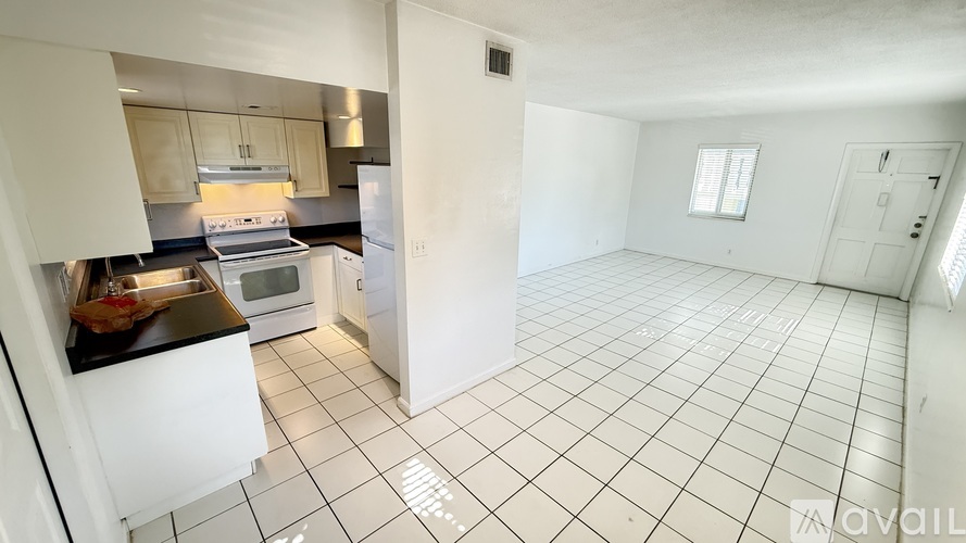 A room with a wooden floor and white walls, with a door on the left and a window on the right.