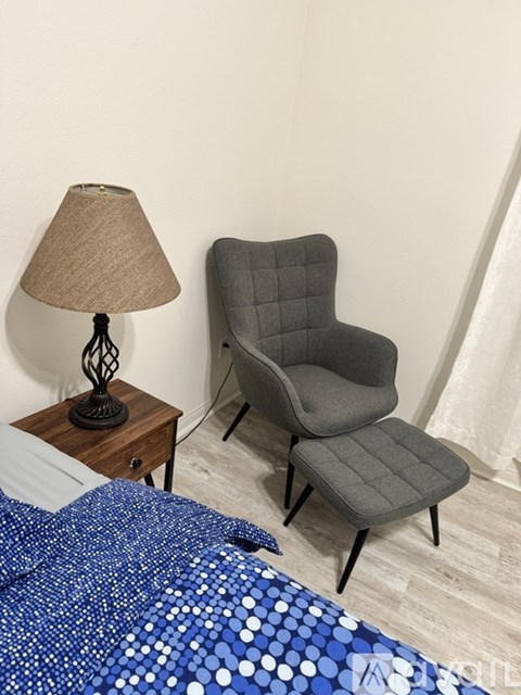 A grey chair sits next to a lamp on a bedroom table.