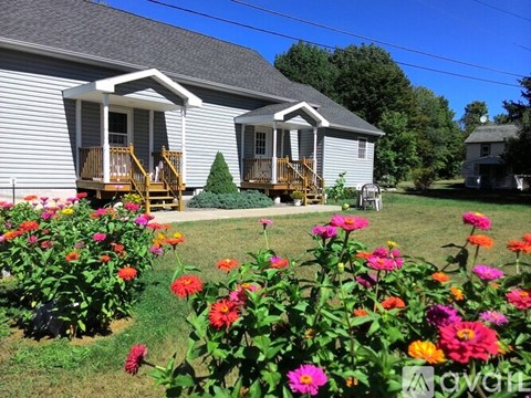 A house with a grey siding and a brown deck is surrounded by a garden with colorful flowers.
