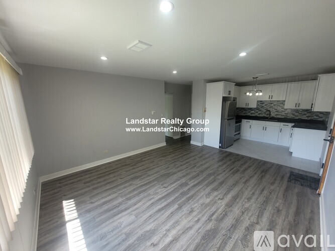A spacious room with wooden flooring and a kitchen area in the background.