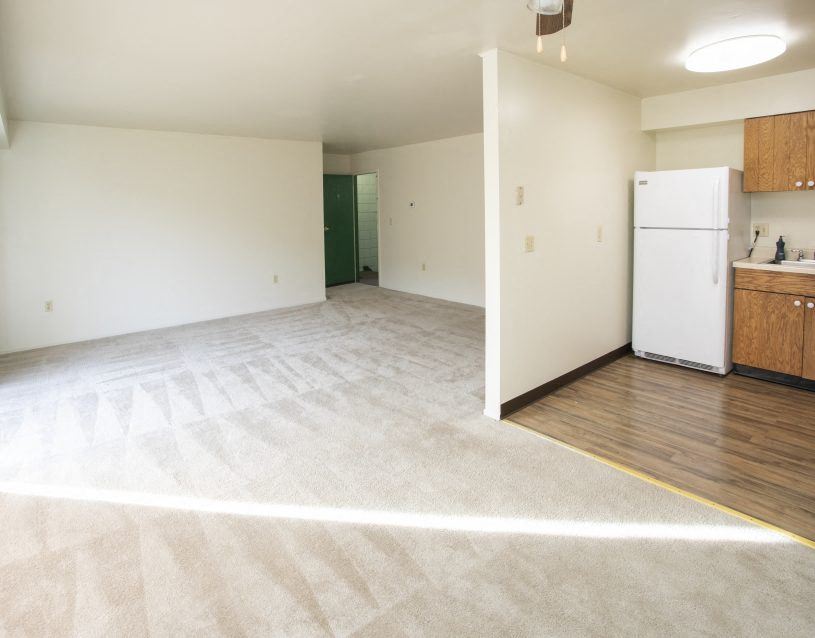 an empty living room and kitchen with a white refrigerator