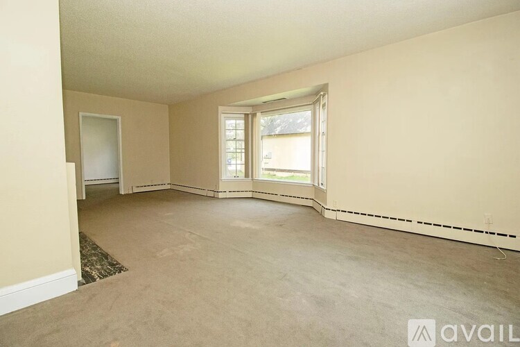 A spacious room with a carpeted floor and a window with blinds.