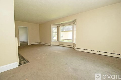 A spacious room with a carpeted floor and a window with blinds.