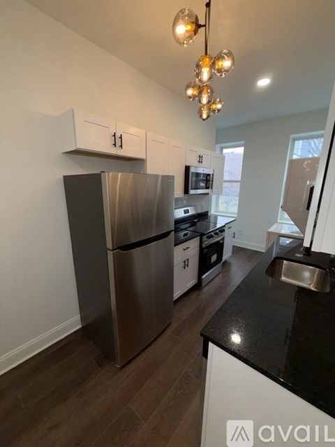 A kitchen with a stainless steel refrigerator and black countertops.