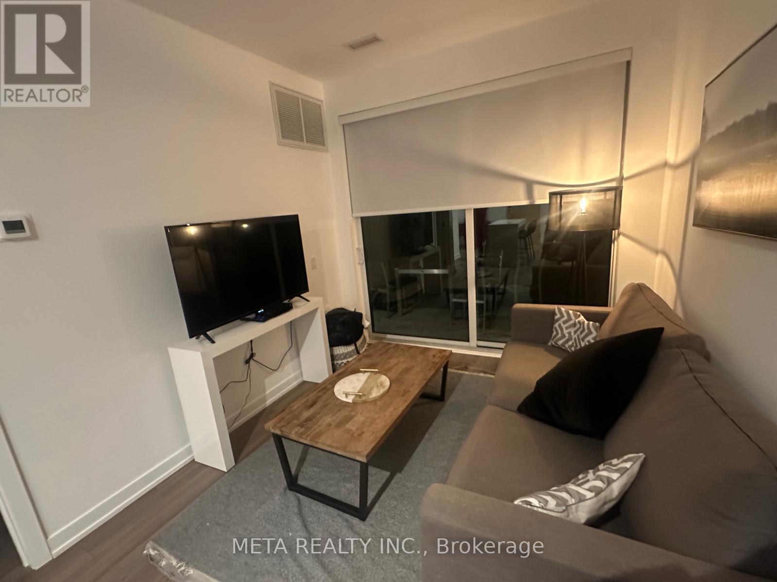 A living room with a grey couch, a wooden coffee table, and a flat screen TV mounted on the wall.