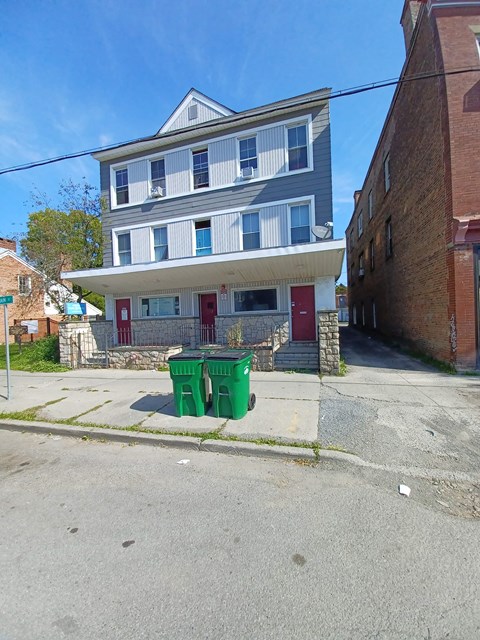 A two-story building with a red door and a green dumpster in front.