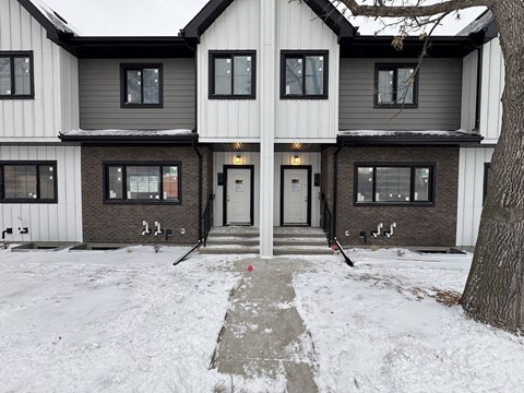 A house with a grey and white exterior and a snow-covered front yard.
