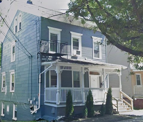 A blue house with a white porch and a tree in front.