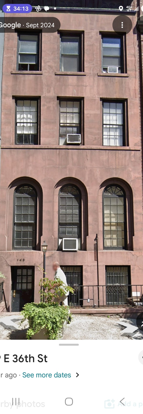 A red brick building with arched windows and a man in a white shirt standing in front of it.