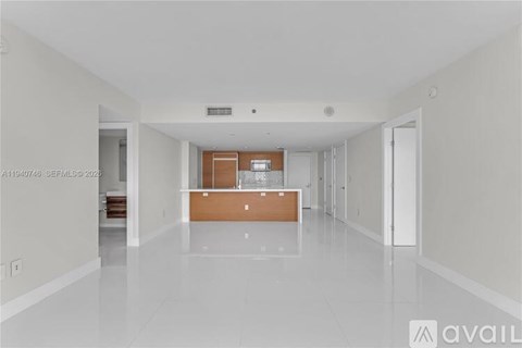 A spacious, empty room with a white floor and walls, and a wooden door in the center.