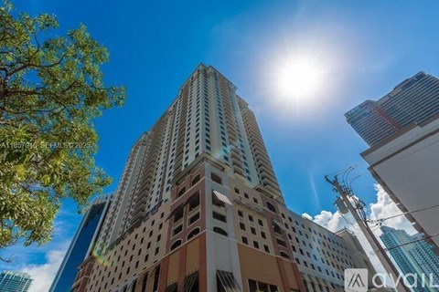 A tall building with many windows and balconies is seen under a bright sun.