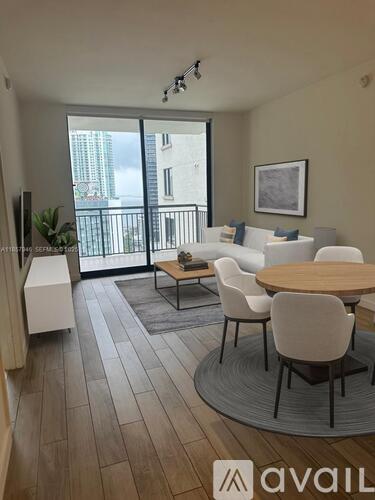 A living room with a dining table and chairs, a balcony with a railing, and a plant.