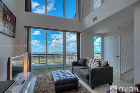A living room with a couch, a television, and a large window overlooking a cityscape.