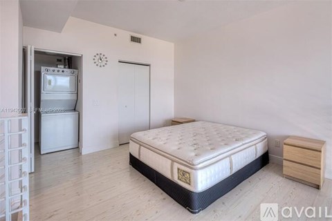 A bedroom with a bed, nightstand, and a small refrigerator.