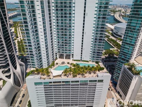 A view of a cityscape with tall buildings and a pool on the roof of one of them.