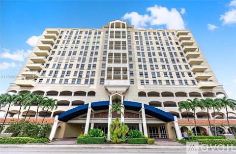 A large, beige hotel with a blue awning and palm trees in front.
