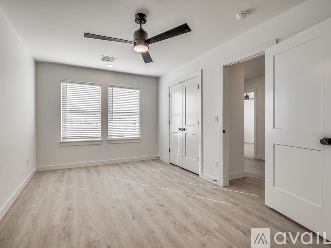 A room with a ceiling fan and light, wooden floors, and white walls with a window.