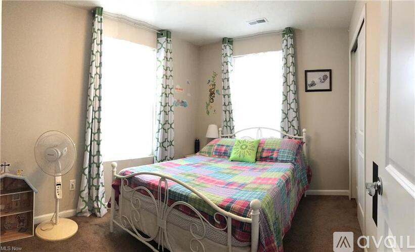 A bedroom with a bed, fan, and window with curtains.