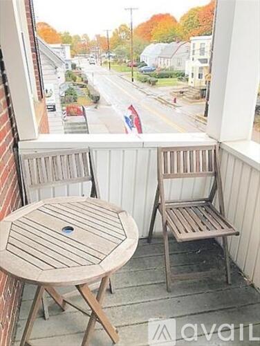 A wooden table and chair are on a balcony overlooking a street.