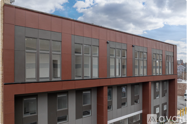 A building with a red and grey facade has a row of windows on the ground floor.