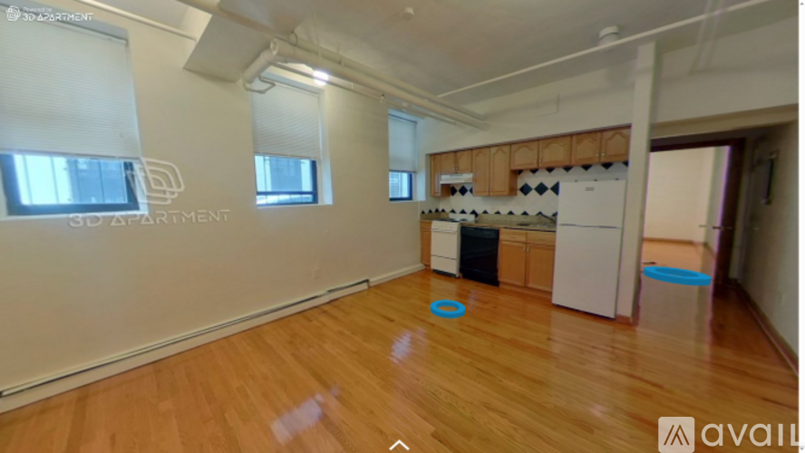 A room with wooden floors and a kitchenette in the background.