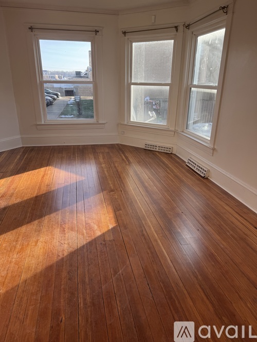 A room with wooden flooring and two windows.