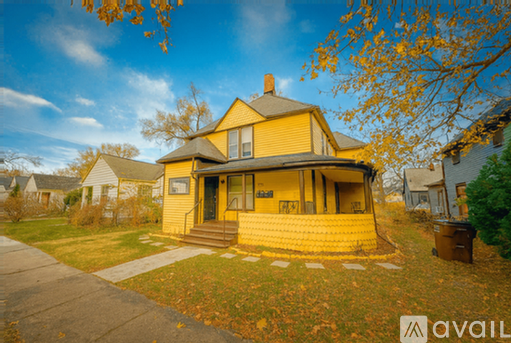 A yellow house with a brown roof and a brown trash can in front of it.
