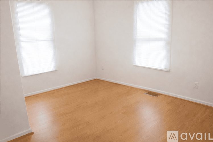 A room with wooden flooring and two windows.