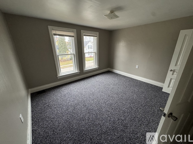 A room with grey carpet and a window overlooking a street.