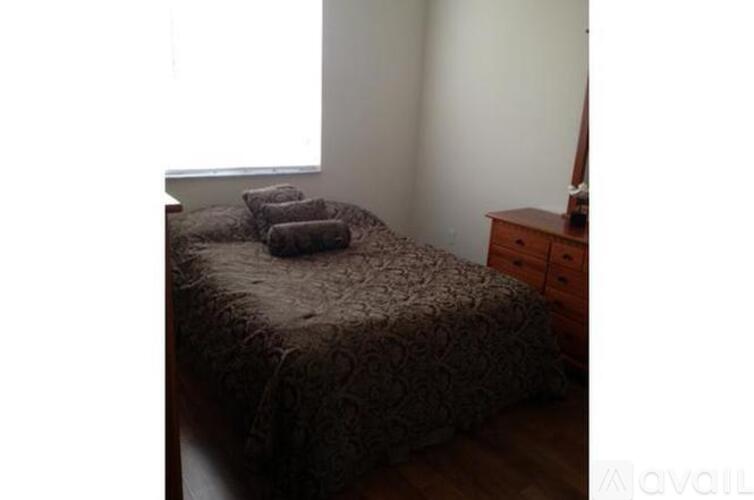 A bed with a brown comforter and two pillows sits in a room with a wooden dresser.