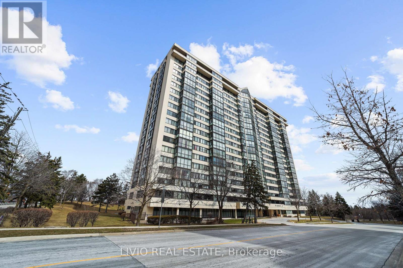 A tall building with many windows is surrounded by trees and grass.