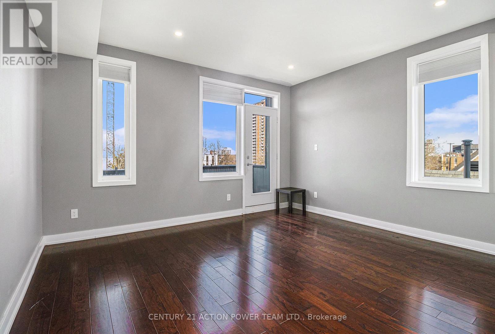 A spacious room with wooden floors and two windows.