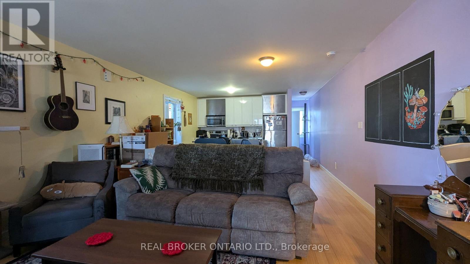 A living room with a grey couch and a guitar hanging on the wall.