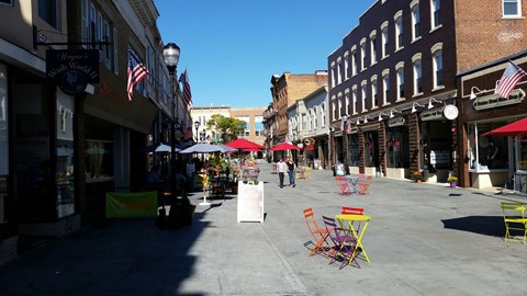 A street view of a town with buildings on either side and a few people walking around.