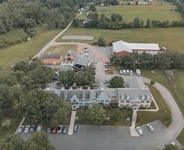 A large white building with a grey roof is surrounded by a parking lot.