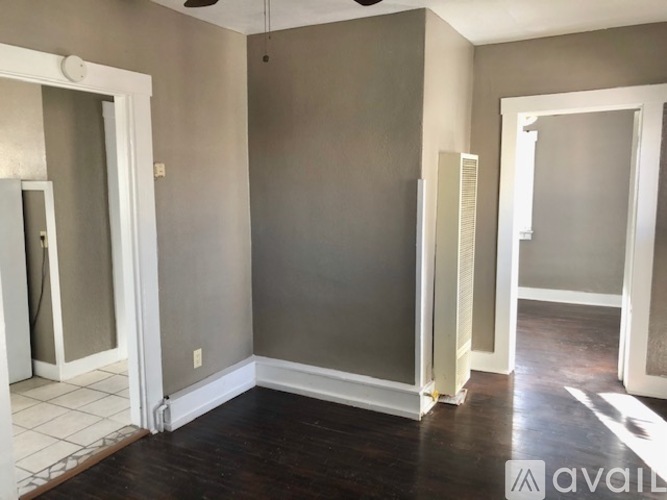 A room with a white door, a grey wall and a wooden floor.