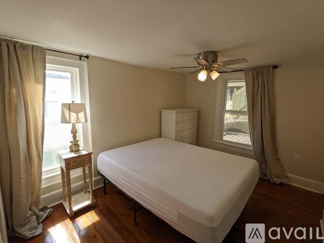 A bedroom with a bed, a small table with a lamp, and a window with curtains.