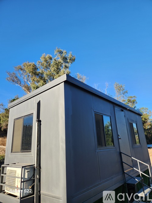 A grey trailer with a ladder and a window is parked outdoors.