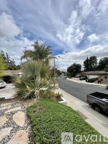 A residential street with a house, trees, and a truck parked on the side.