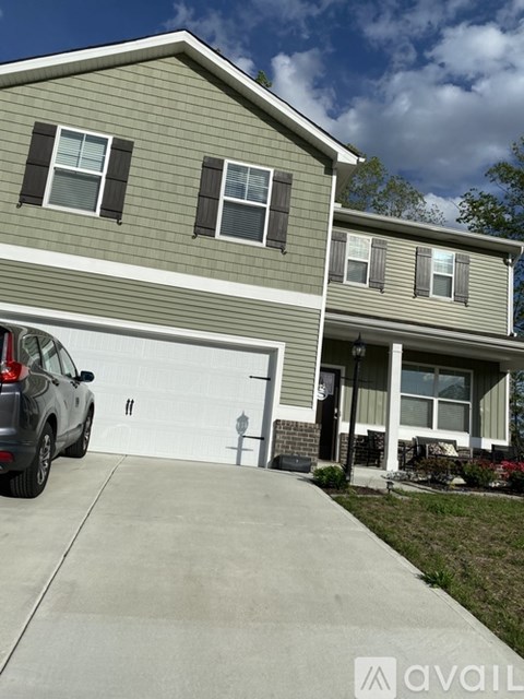 A grey car is parked in front of a grey house.