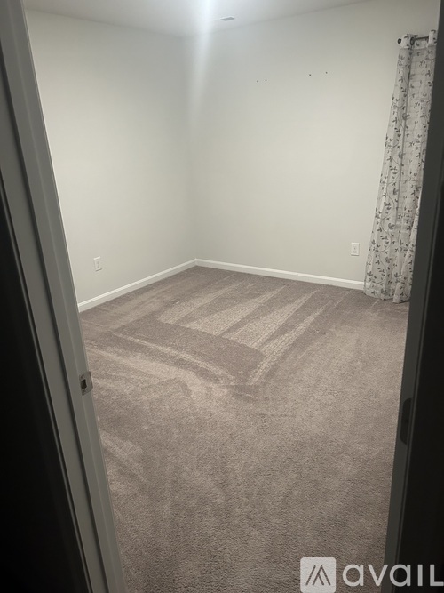 A carpeted room with a curtain on the window.