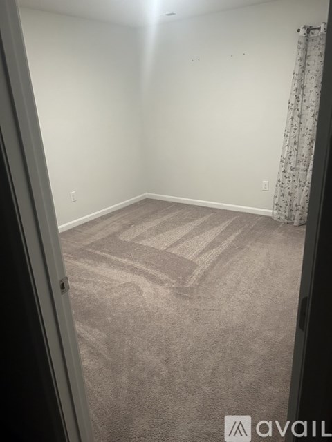 A carpeted room with a curtain on the window.