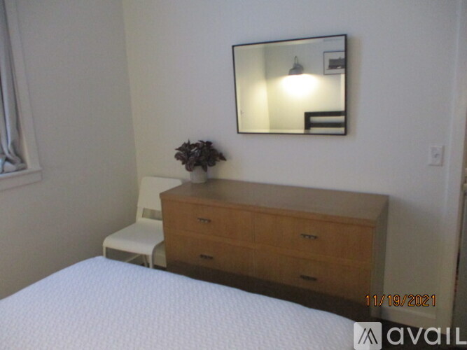 A bedroom with a bed, a chair, a mirror and a wooden dresser.
