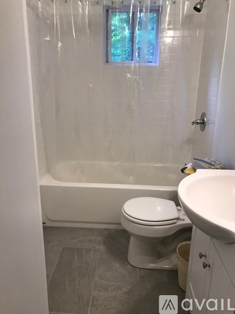 A white toilet is in a bathroom with a white tub and sink.